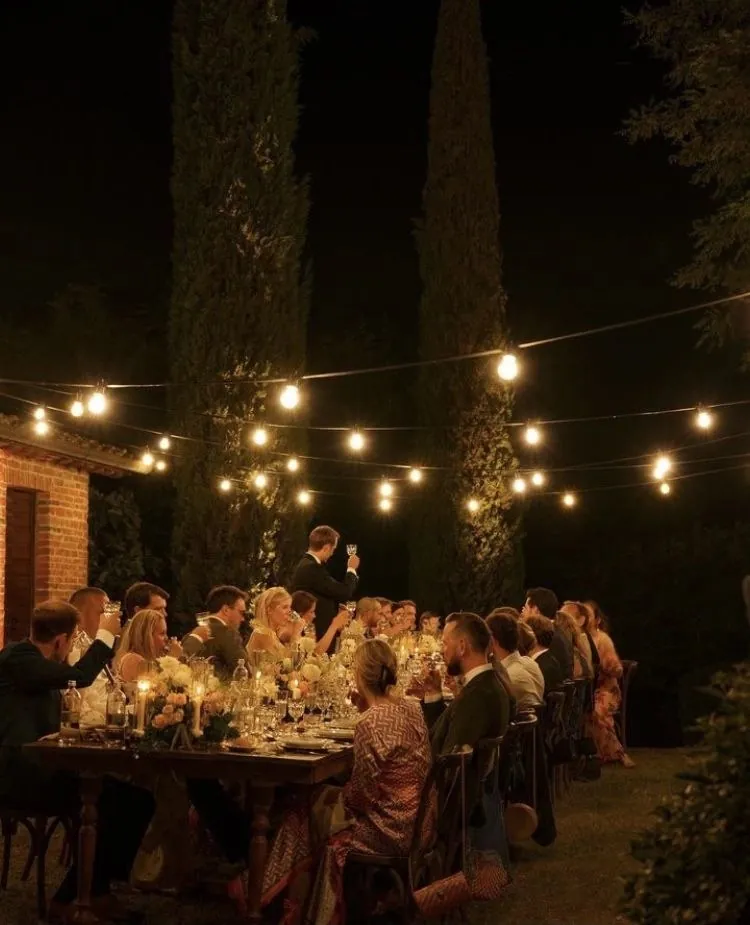 Cena de boda al aire libre entre cipreses, bajo guirnaldas de bombillas