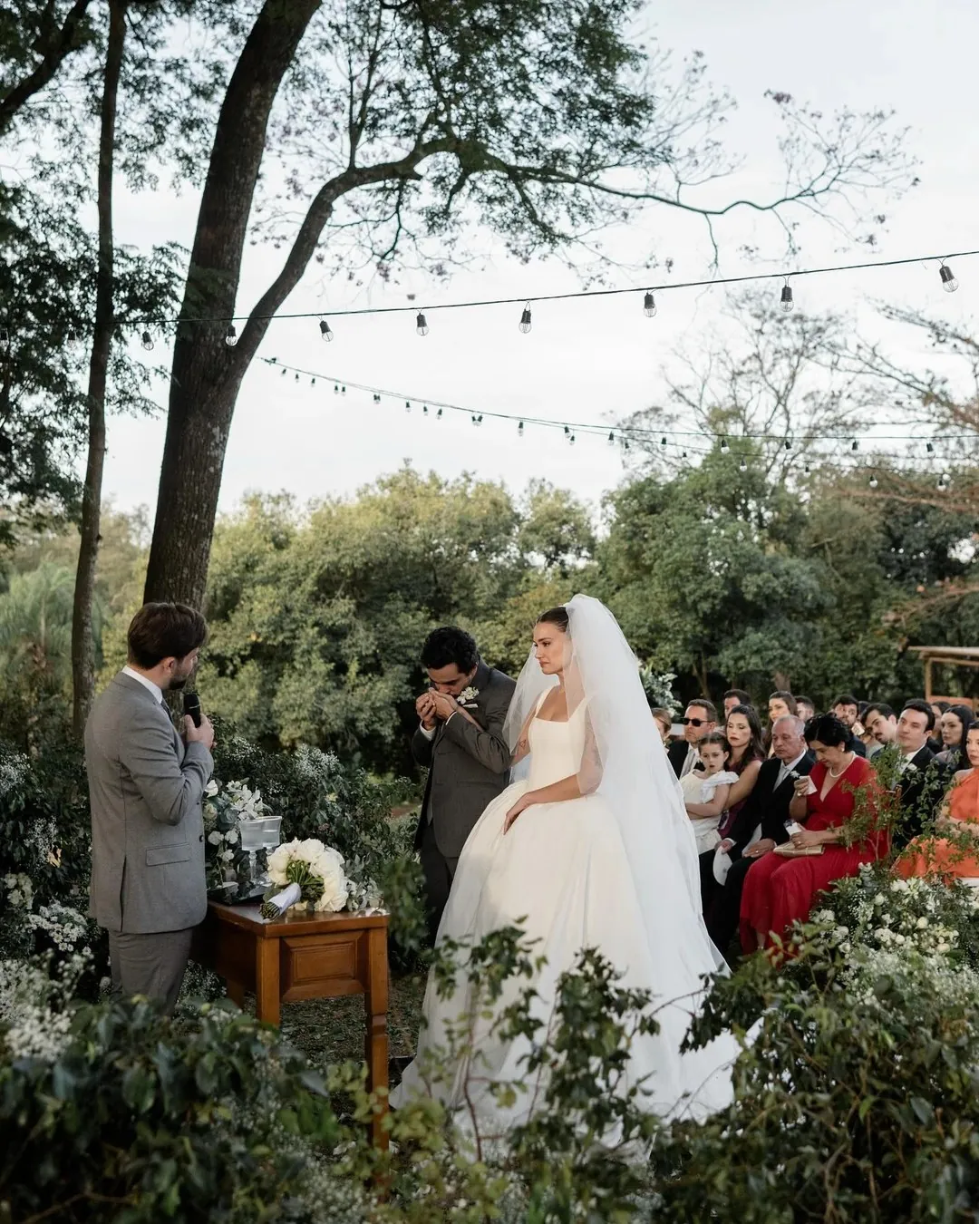 Ceremonia de boda al aire libre: el oficiante con micrófono, los novios emocionados y los invitados bajo guirnaldas de bombillas