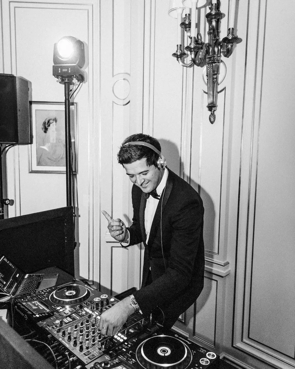 DJ de esmoquin y cascos mezclando en blanco y negro entre foco y altavoz