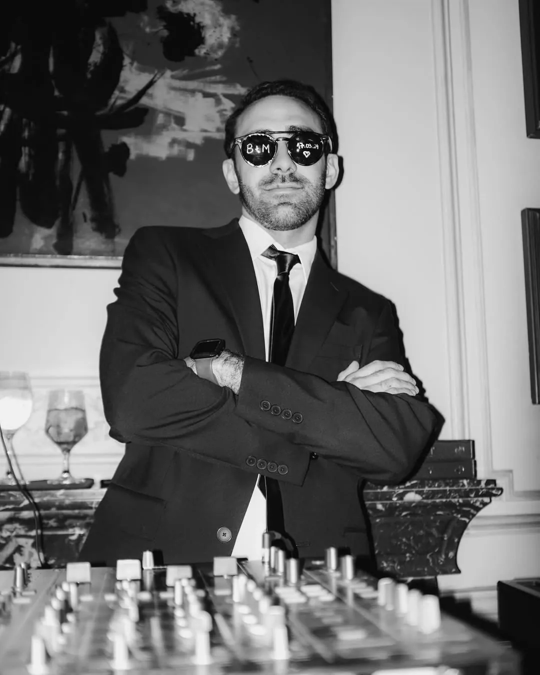 DJ de traje y gafas de sol personalizadas, con los brazos cruzados detrás de la mesa de mezclas